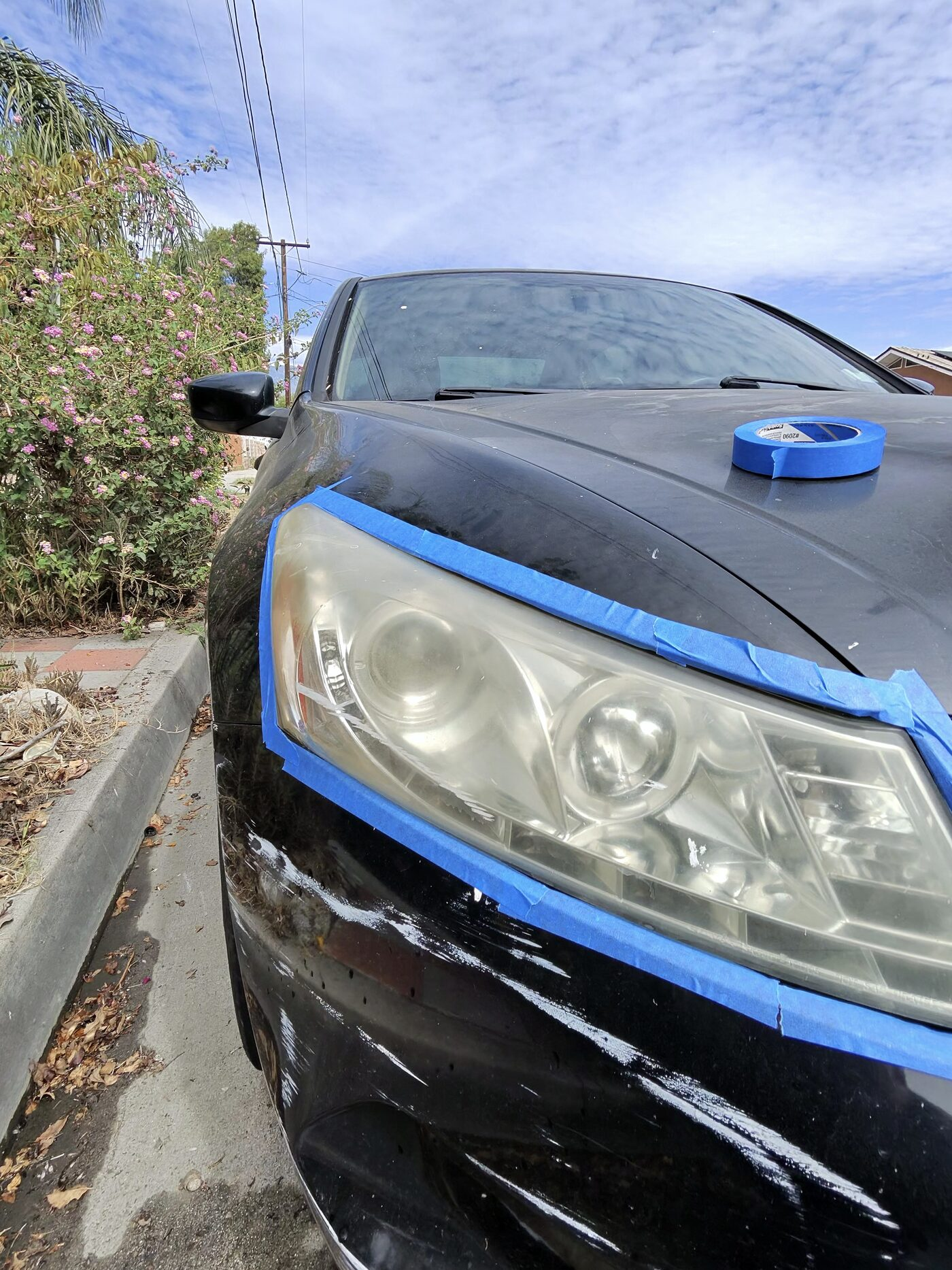 Before: yellowed, hazy passenger-side headlight on a black sedan, taped off